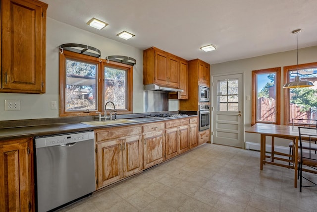 kitchen with a sink, under cabinet range hood, dark countertops, appliances with stainless steel finishes, and light floors