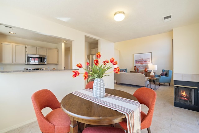 dining space with light tile patterned floors, visible vents, and a tile fireplace