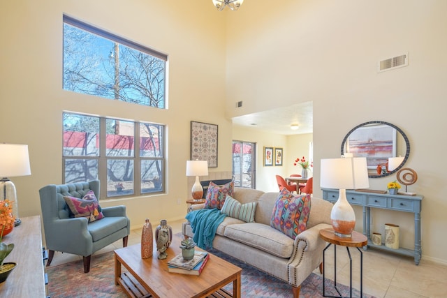 living area with light tile patterned floors, visible vents, a high ceiling, and baseboards