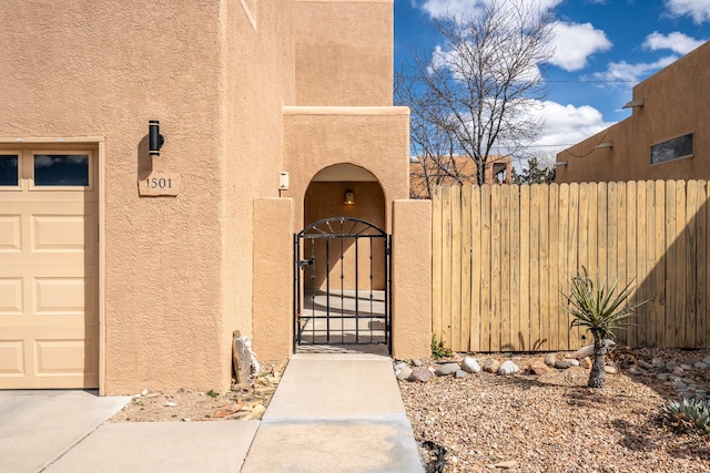 entrance to property featuring a gate, stucco siding, and fence