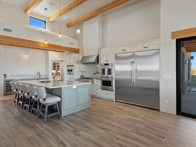 kitchen with visible vents, a sink, wine cooler, appliances with stainless steel finishes, and wall chimney exhaust hood