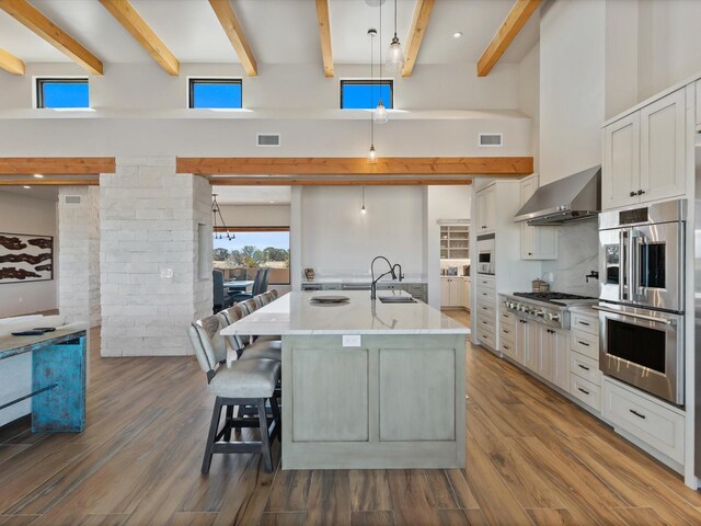 kitchen featuring a center island with sink, wood finished floors, hanging light fixtures, wall chimney exhaust hood, and a sink