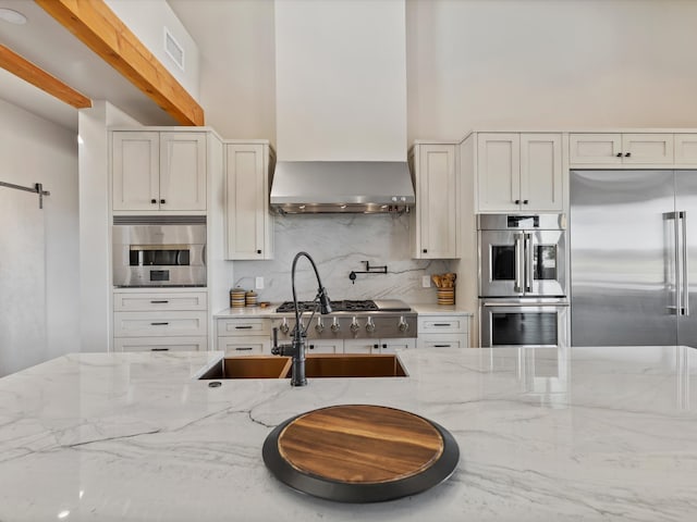 kitchen with visible vents, appliances with stainless steel finishes, wall chimney exhaust hood, and light stone countertops