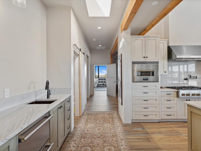 kitchen featuring a sink, stainless steel appliances, a barn door, wall chimney exhaust hood, and a skylight