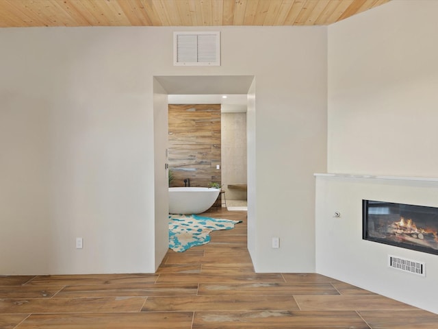 unfurnished living room featuring visible vents, wood finished floors, wood ceiling, and a glass covered fireplace