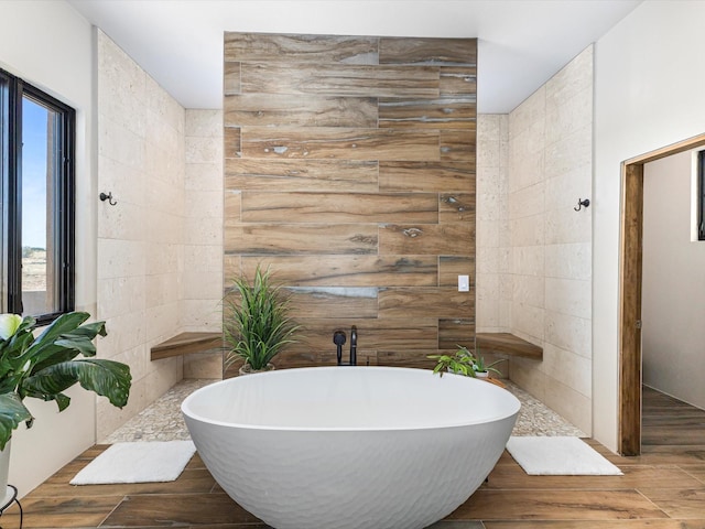 full bath featuring a freestanding tub, tile walls, and wood finished floors