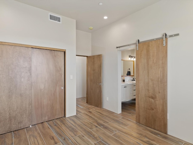 unfurnished bedroom with visible vents, wood finish floors, a barn door, ensuite bathroom, and a closet