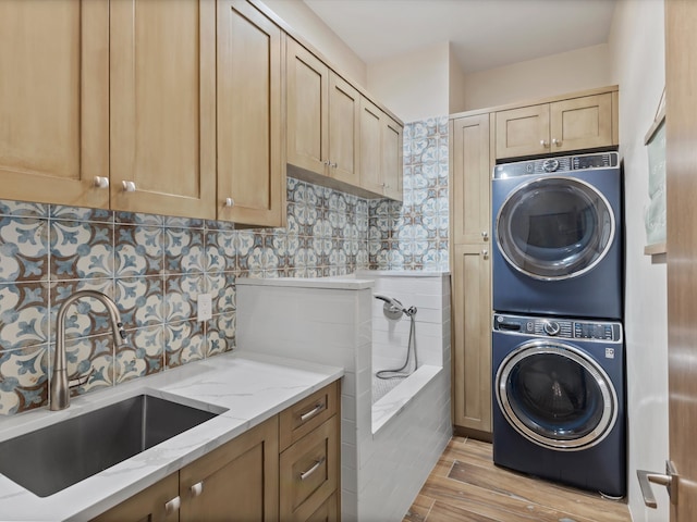 laundry room featuring cabinet space, stacked washer and dryer, light wood-style flooring, and a sink