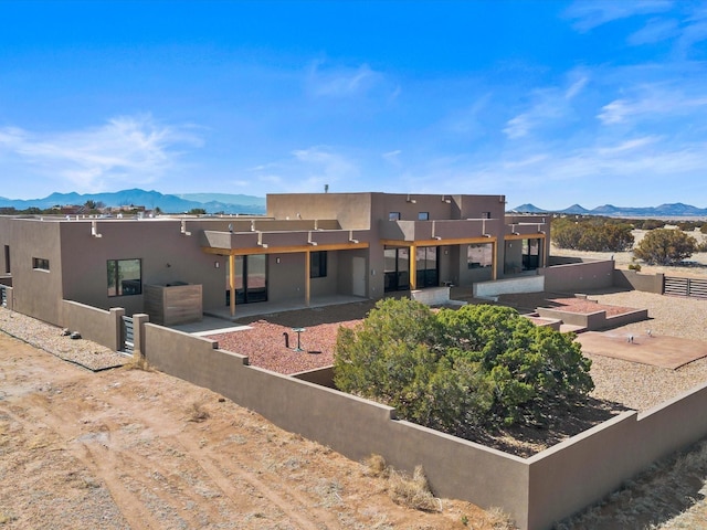 back of property with fence, a patio area, a mountain view, and stucco siding