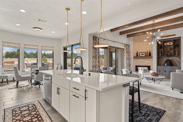 kitchen with visible vents, beam ceiling, a kitchen island with sink, a sink, and a textured ceiling