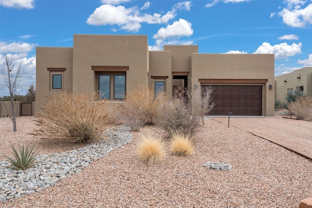 pueblo-style home featuring stucco siding, a garage, and driveway