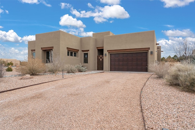 pueblo-style home with stucco siding, an attached garage, and dirt driveway