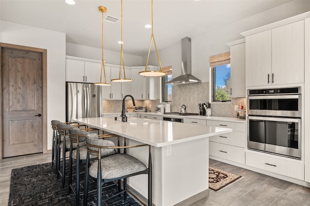 kitchen featuring visible vents, appliances with stainless steel finishes, a kitchen breakfast bar, exhaust hood, and tasteful backsplash