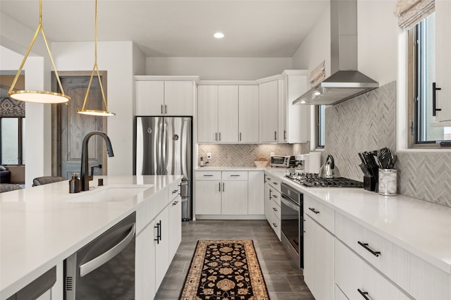 kitchen with backsplash, wall chimney range hood, light countertops, appliances with stainless steel finishes, and a sink