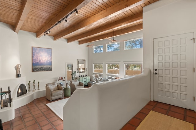 tiled living area with beamed ceiling, rail lighting, wood ceiling, and a lit fireplace