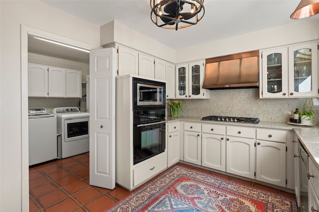 kitchen with tile patterned floors, premium range hood, washing machine and dryer, white cabinetry, and appliances with stainless steel finishes