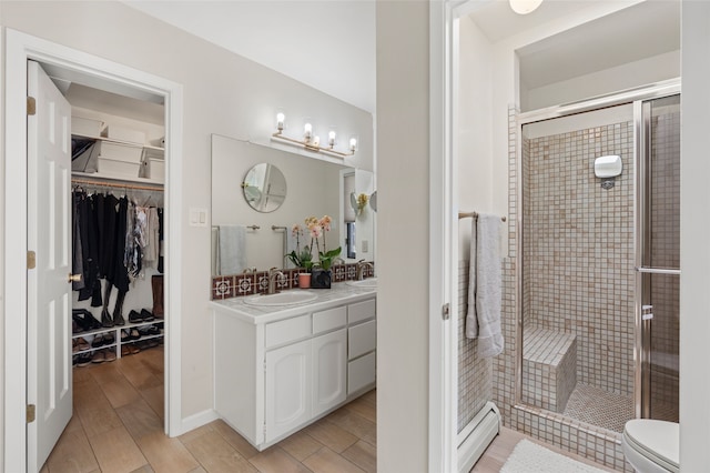 bathroom featuring a shower stall, a walk in closet, wood finish floors, toilet, and vanity