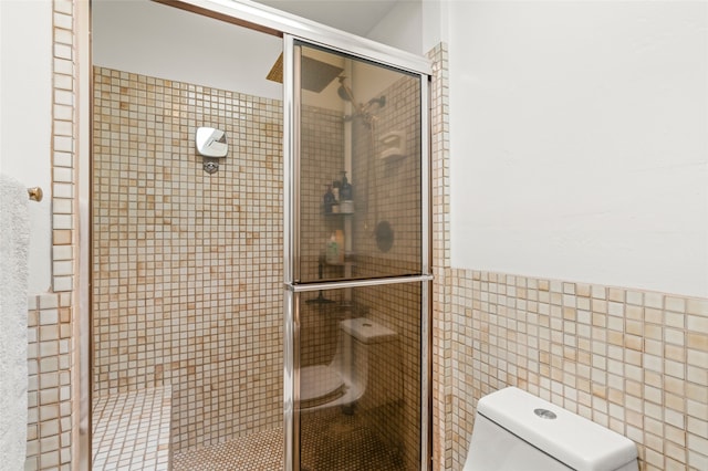 full bathroom featuring a wainscoted wall, toilet, tile walls, and a shower stall