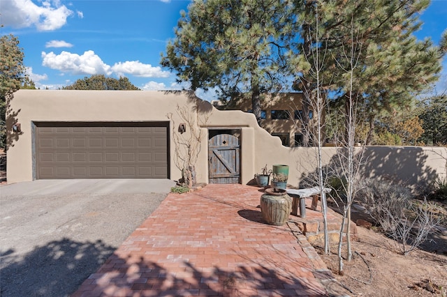 pueblo-style house with a gate, fence, an attached garage, and stucco siding