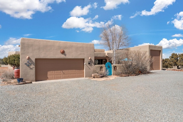 pueblo-style house with gravel driveway, a garage, and stucco siding