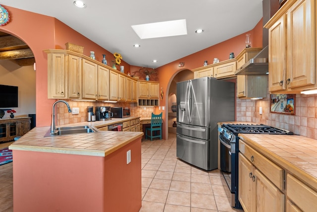 kitchen with a sink, stainless steel appliances, tile counters, and light brown cabinetry