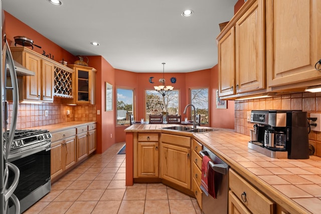 kitchen featuring tile counters, light tile patterned floors, appliances with stainless steel finishes, a peninsula, and a sink