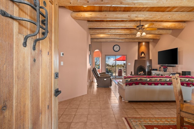 tiled living room with beam ceiling, wooden ceiling, a large fireplace, and a ceiling fan