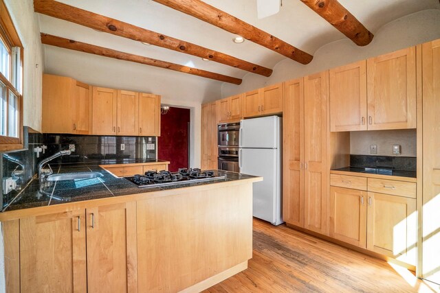 kitchen with gas cooktop, a peninsula, freestanding refrigerator, light brown cabinetry, and tile counters