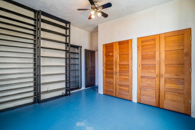 unfurnished bedroom featuring a ceiling fan, concrete floors, and multiple closets