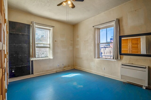 empty room with a wealth of natural light, baseboards, heating unit, and ceiling fan