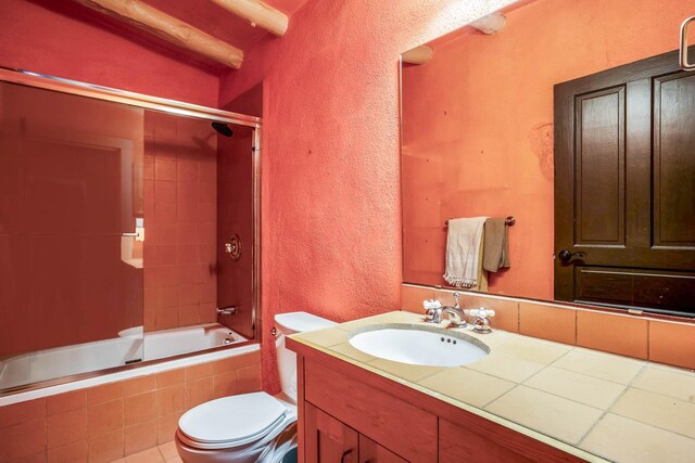 full bath featuring toilet, vanity, tiled shower / bath, and a textured wall