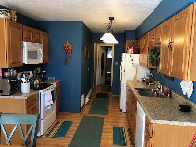 kitchen featuring white appliances, light wood finished floors, a sink, light countertops, and a textured ceiling