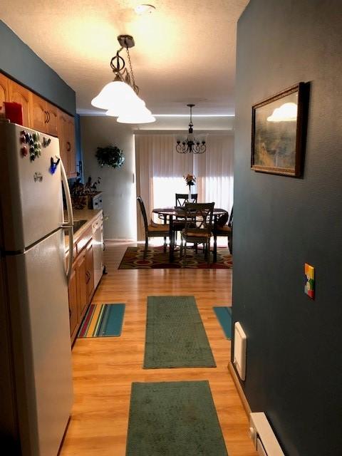 kitchen with light wood-style flooring, brown cabinetry, freestanding refrigerator, and pendant lighting