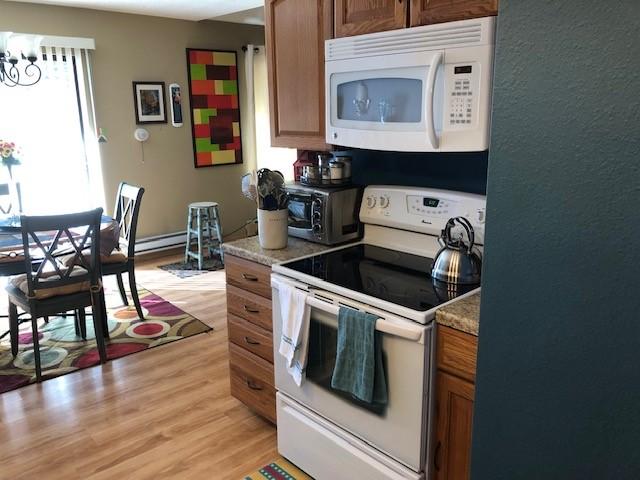 kitchen featuring a notable chandelier, white appliances, a toaster, brown cabinetry, and light wood finished floors