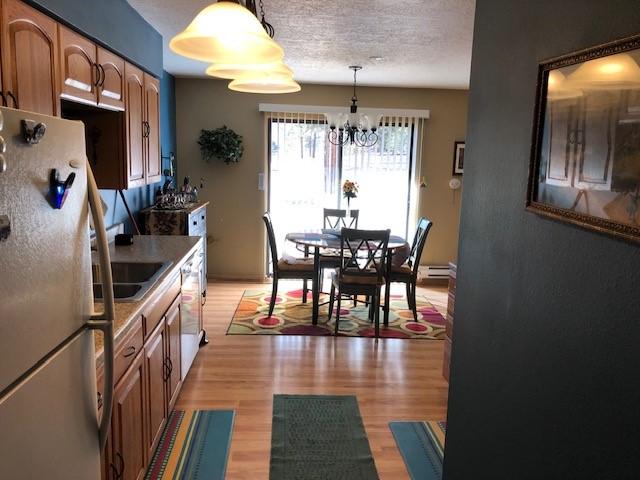 kitchen with dishwashing machine, freestanding refrigerator, a textured ceiling, light wood-type flooring, and a chandelier