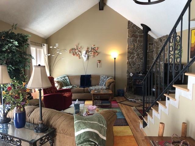 living room featuring stairway, wood finished floors, high vaulted ceiling, beam ceiling, and a wood stove