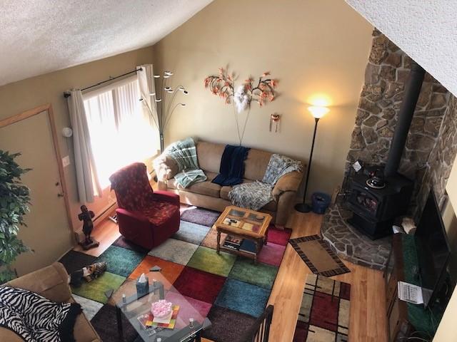 living area with lofted ceiling, a textured ceiling, wood finished floors, and a wood stove