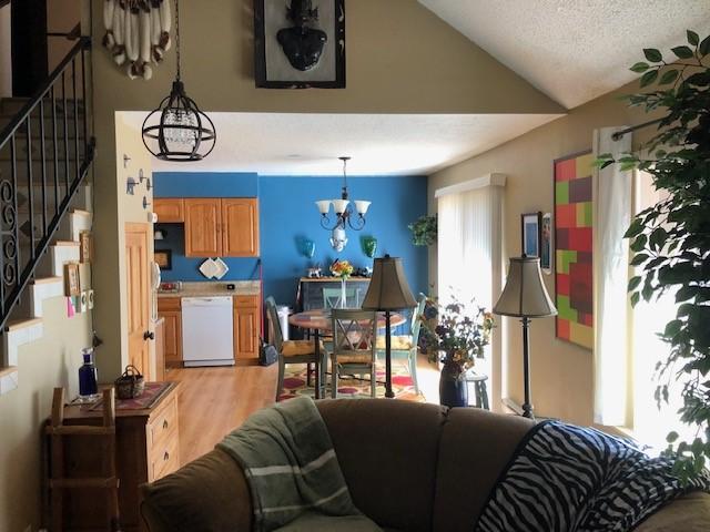 living area with stairs, vaulted ceiling, light wood-style floors, a textured ceiling, and a notable chandelier