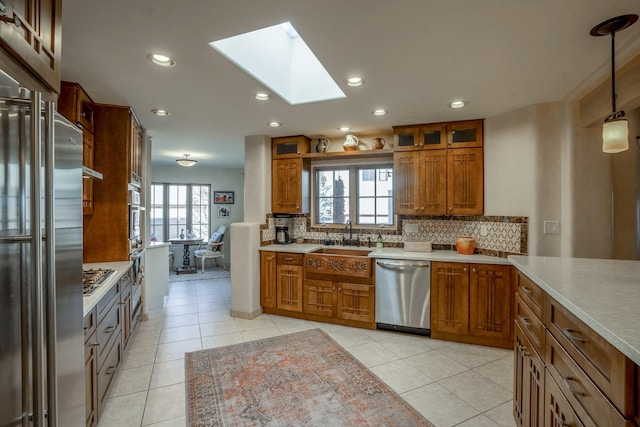 kitchen with decorative backsplash, a skylight, brown cabinetry, and appliances with stainless steel finishes