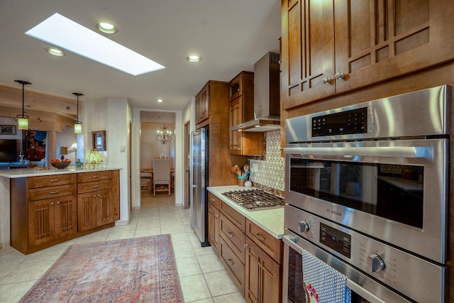 kitchen with brown cabinets, appliances with stainless steel finishes, and wall chimney range hood