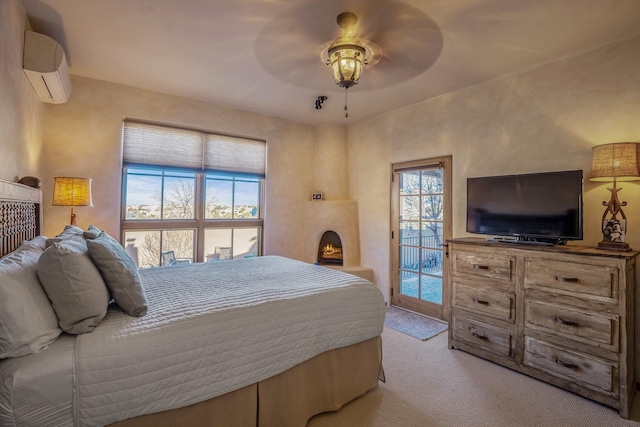 carpeted bedroom featuring a warm lit fireplace, access to exterior, a ceiling fan, and a wall unit AC