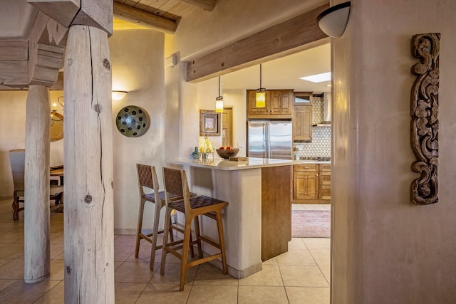 kitchen with beamed ceiling, built in refrigerator, light countertops, light tile patterned floors, and decorative backsplash