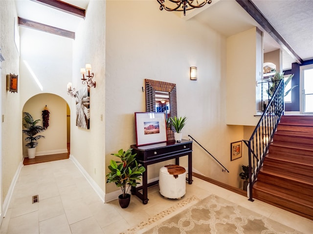 interior space featuring tile patterned flooring, visible vents, baseboards, beam ceiling, and arched walkways