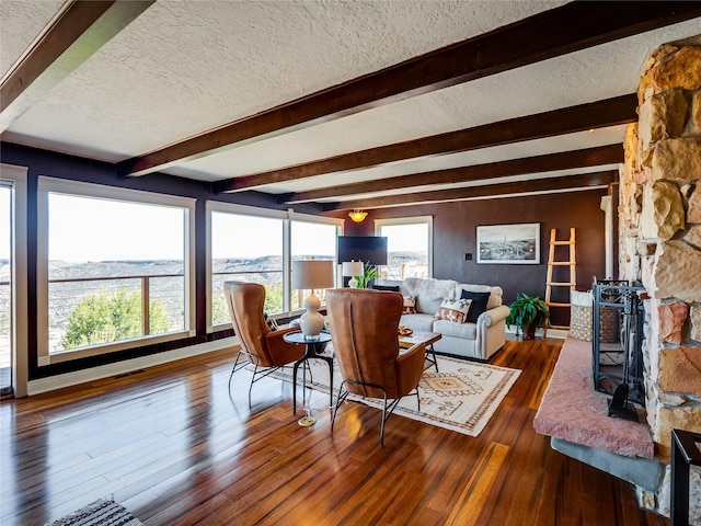 living room featuring beam ceiling, a textured ceiling, a wood stove, and hardwood / wood-style flooring