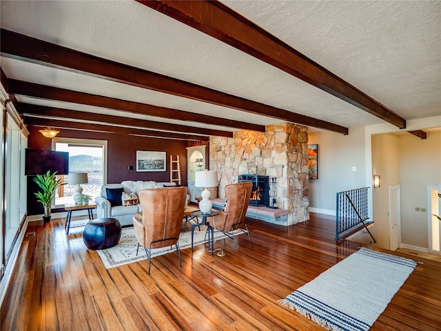 living room featuring baseboards, a textured ceiling, hardwood / wood-style floors, and a fireplace