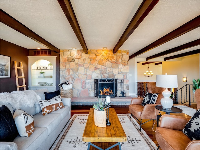 living area with wood finished floors, beam ceiling, a stone fireplace, a textured ceiling, and a chandelier