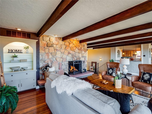 living area featuring beam ceiling, a textured ceiling, a stone fireplace, and wood finished floors