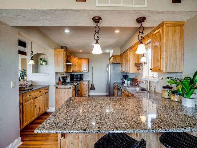 kitchen with visible vents, a peninsula, stone countertops, a sink, and appliances with stainless steel finishes