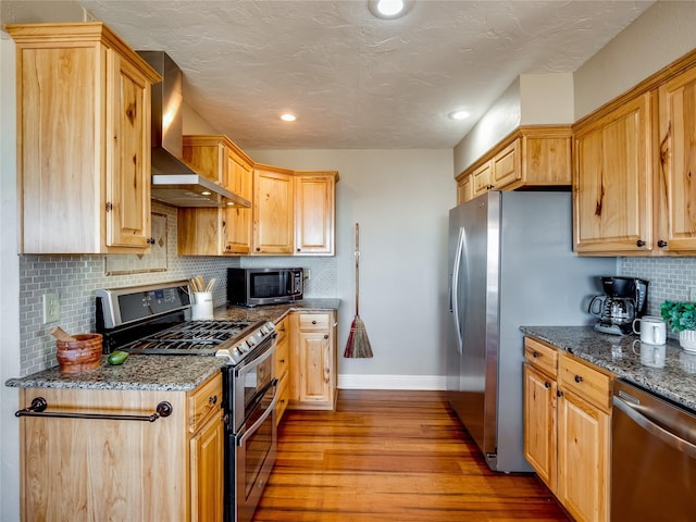 kitchen featuring tasteful backsplash, wood finished floors, stainless steel appliances, wall chimney exhaust hood, and baseboards