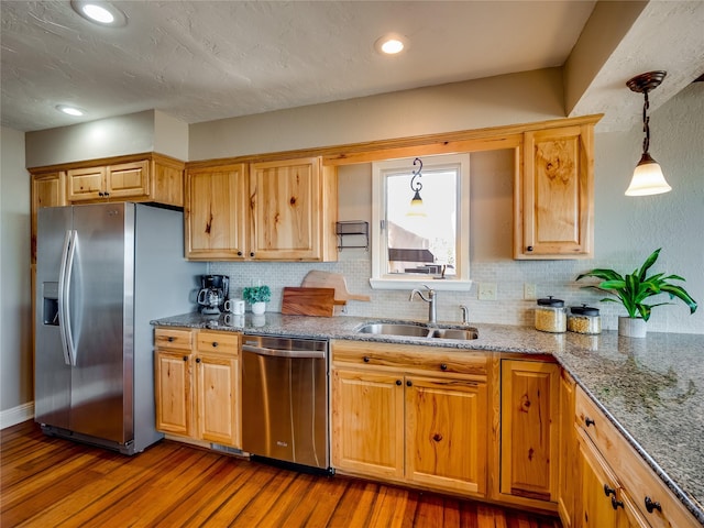 kitchen with a sink, wood finished floors, stainless steel appliances, stone counters, and decorative backsplash